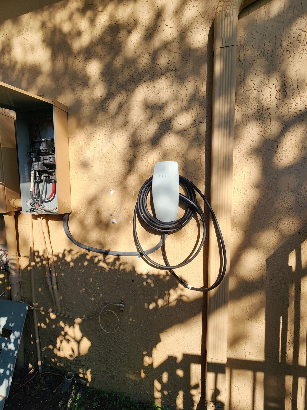 Wall-mounted EV charger with its cable coiled, installed beside an exterior panel